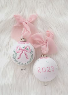 two ornaments with pink bows on them sitting on a white fur covered floor next to each other