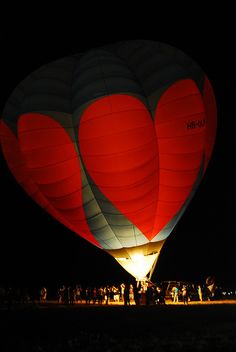 two hot air balloons in the shape of hearts are lit up at night as people look on