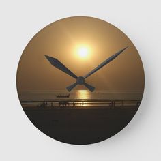 a clock with the sun setting behind it and people walking on the beach in the distance