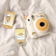 a polaroid camera sitting on top of a bed next to two small stickers