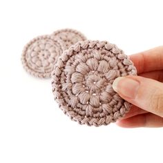 two crocheted coasters in the shape of flowers are being held by a person's hand