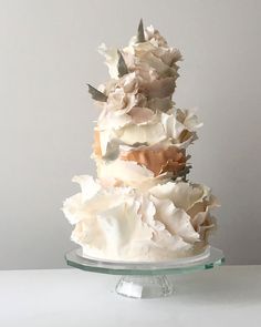 a three tiered cake with white frosting and flowers on the top is sitting on a glass platter