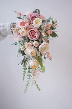 a person holding a bouquet of pink and white flowers with greenery on the side