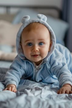 a baby laying on top of a bed wearing a blue outfit