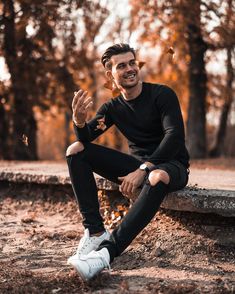 a man sitting on a stone bench in the park with his hands together and smiling