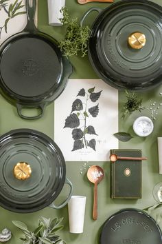 an assortment of green dishes and utensils laid out on a table with greenery