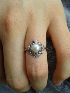 a close up of a person's hand with a pearl ring on their finger