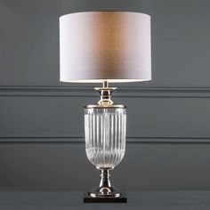 a clear glass table lamp with a white shade on the base and a light brown drum