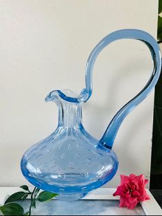 a blue glass vase sitting on top of a table next to a pink flower and green leaves