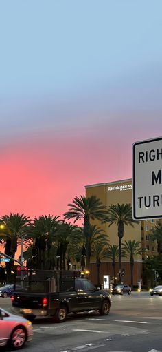 a street sign on the side of a road with palm trees and buildings in the background