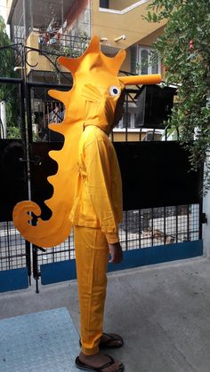 a man in a yellow suit is standing on the sidewalk with a large seahorse costume