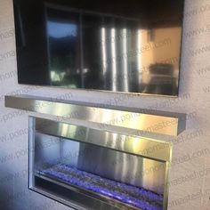 a stainless steel fire place with blue water in the bottom and an empty mirror above it