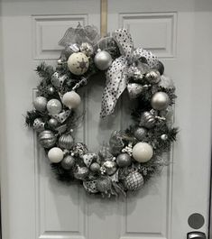 a christmas wreath hanging on the front door with silver and white ornaments around it's edges