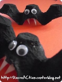 two black bats with googly eyes and fangs on them, sitting in front of an orange background