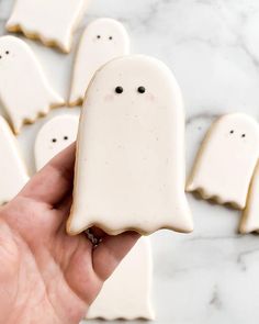 a hand holding a white cookie shaped like a ghost