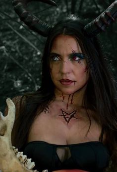 a woman with long hair and horns on her head is holding a skull in front of her face