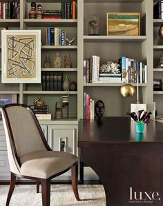 a chair sitting in front of a desk with bookshelves behind it and an art work on the wall