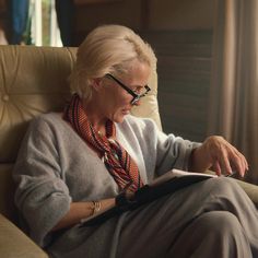 an older woman sitting in a chair reading a book