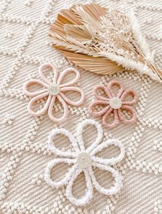 three crocheted flowers sitting on top of a white blanket next to a basket