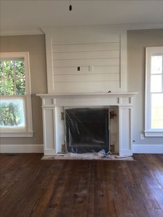 an empty living room with hard wood flooring and white painted fireplace mantels