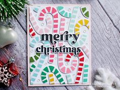 a merry christmas card with candy canes and ornaments on the table next to it