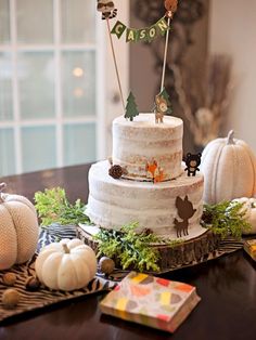 a three tiered cake sitting on top of a wooden table next to white pumpkins