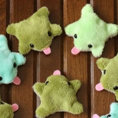 six stuffed animals are arranged on a wooden surface, one is green and the other is blue