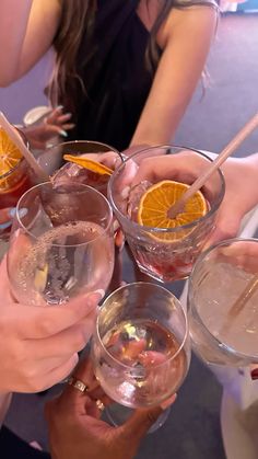 several people are holding glasses with orange slices in them