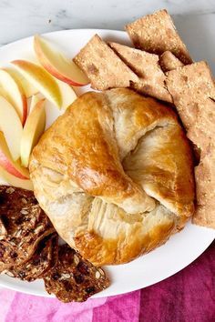 a white plate topped with apple slices and pastries next to crackers on a pink towel