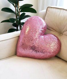 a pink heart shaped pillow sitting on top of a white couch next to a potted plant