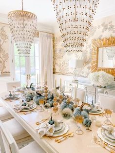 a dining room table is set with white dishes and place settings, gold chargers on the chandelier