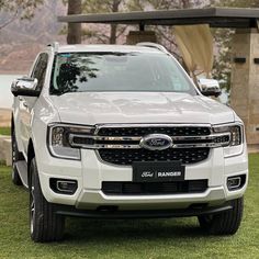 the front end of a white truck parked on top of a lush green field next to a lake