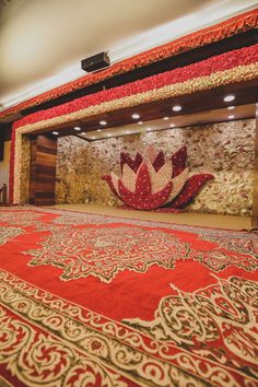 a large red and gold rug with a flower on it in front of a wall