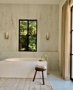 a large white bath tub sitting next to a window in a bathroom with marble walls and floors