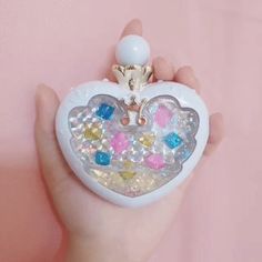 a hand holding a small white heart shaped box with colorful jewels on the front and sides