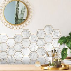 a desk with a mirror, pen holder and plant on it in front of a marble hexagonal wall