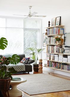 a living room filled with furniture and bookshelves next to a window covered in plants