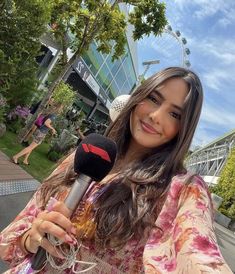 a woman holding a microphone in her hand and smiling at the camera while standing outside