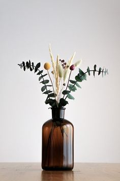 a vase filled with lots of flowers on top of a wooden table in front of a white wall