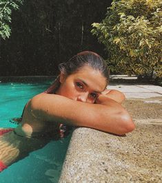 a woman is swimming in the pool with her hands on her head and looking at the camera