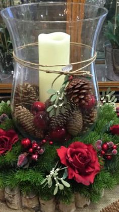 a glass vase filled with pine cones and red flowers sitting on top of a table