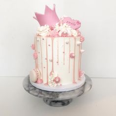 a white and pink cake with flowers on top sitting on a marble stand in front of a white wall