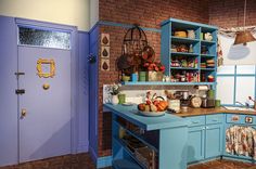 a kitchen with blue cabinets and wooden counter tops in front of a brick wall that has an open door