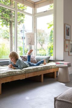 a young boy laying on top of a bed in front of a window reading a book