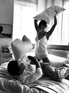 two people laying on top of a bed with pillows in the air and one person holding up a pillow