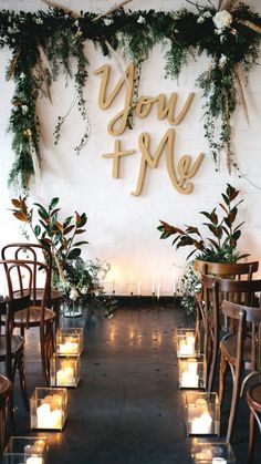 an aisle with candles and greenery on the wall, decorated with wooden letters that read you me