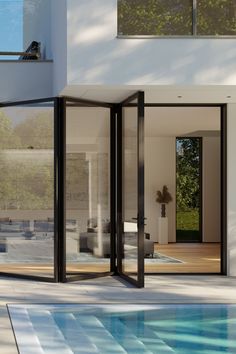 an empty swimming pool in front of a white house with glass walls and sliding doors