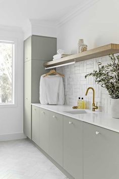 a kitchen with white tile and green cabinets, gold faucet, sink, towel rack and window