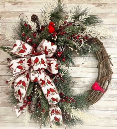 a wreath with red birds and pine cones is hung on a wooden wall next to a bird ornament