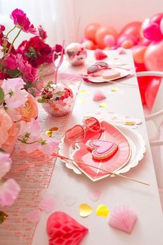 the table is set with pink and red balloons, plates, cups, and vases